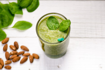 Spinach smoothie on a wooden white background. Glass of smoothie with two leaves of spinach. Nuts. Healthy food. Breakfast.