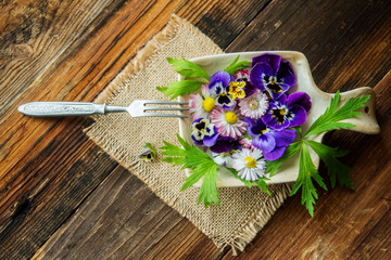 Fresh salad with smoked salmon, black olives, cherry tomatoes and edible flowers on wooden background.