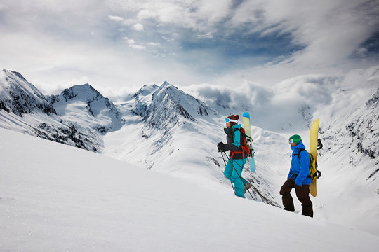 Young people climbing to top of mountain carrying ski equipment