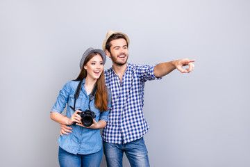 Naklejka premium Check this out! Happy young couple of tourists are on vacation, in casual outfits, hats and with camera, isolated on pure background