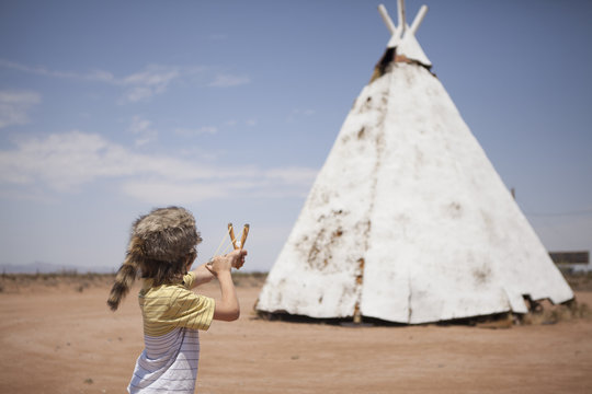 Boy aiming slingshot at teepee, Indian Reservation, USA