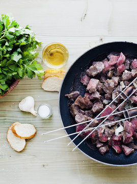 Skewers and meat cooking in pan