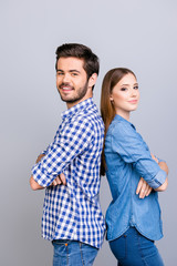 Two cheerful young lovers are looking at the camera and smile, standing back to back, wearing casual clothes, with crossed hands on the pure background