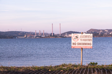 Fototapeta na wymiar No Swimming sign by the beach, with power plant station in the background. Lavrio, Greece.