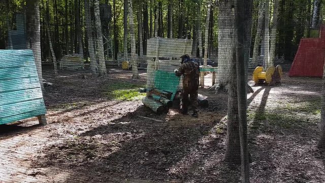 Man in uniform and mask with gun in hand runs in ambush hiding from enemy while playing paintball