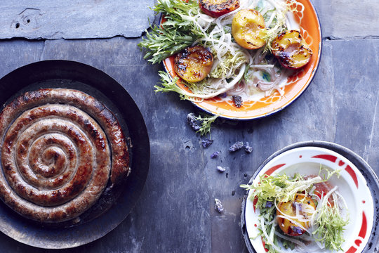 Toulouse sausage in frying pan with plates of peach salad