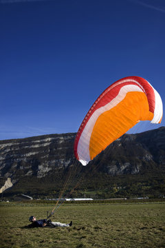 Mature male paraglider lying on back with parachute, Mount Saleve, Geneva, Switzerland