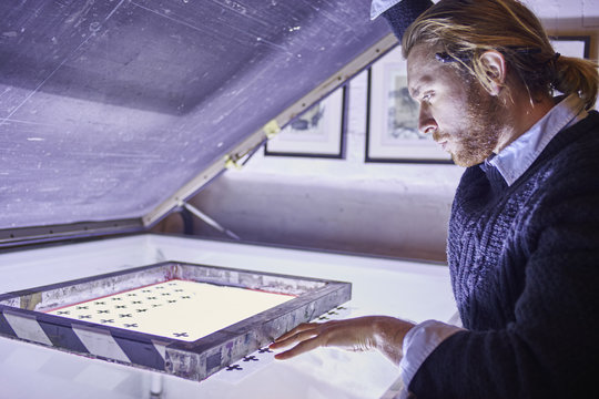 Young man preparing screen on lightbox in traditional print workshop