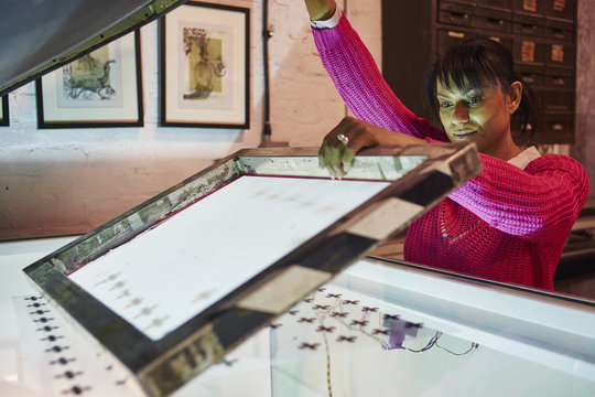 Mid adult woman preparing screen on lightbox in traditional print workshop