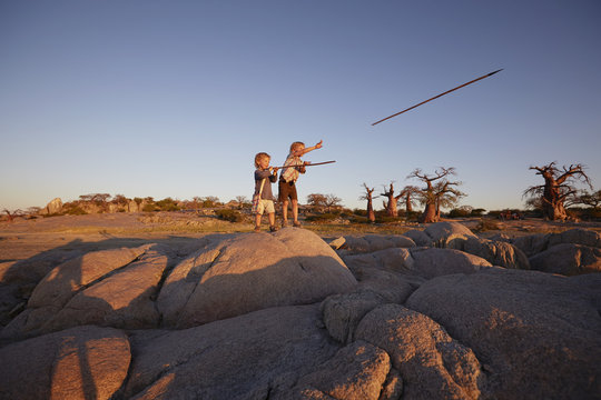 Two young boys standing on rock, throwing spears, Gweta, makgadikgadi, Botswana