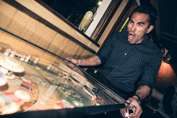 Young man playing pinball in bar, excited expression