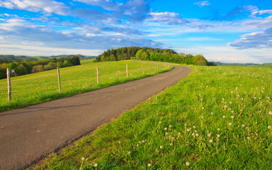 Road in field with clouds and sun.