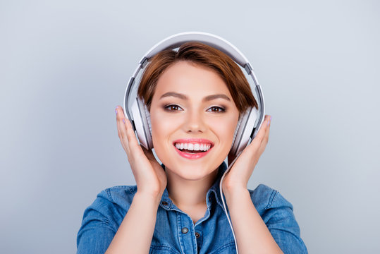 Cheerful young girl is listening to music in big white earphones on pure blue background
