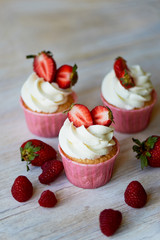 Cupcakes with whipped cream and sweet cream, decorated with strawberries.On a light wooden background.