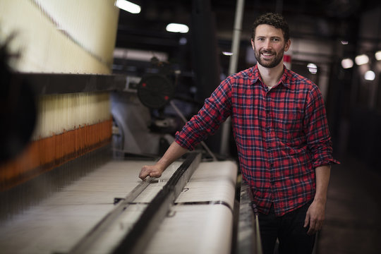 Portrait of young male weaver using old weaving machine in textile mill