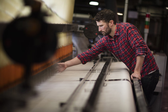 Young male weaver using old weaving machine in textile mill