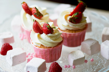 Cupcakes with whipped cream and sweet cream, decorated with strawberries.On a glass stand, with marshmallows