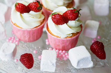 Cupcakes with whipped cream and sweet cream, decorated with strawberries.On a glass stand, with marshmallows