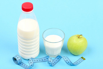 Milk and apple near tape for measuring on blue background