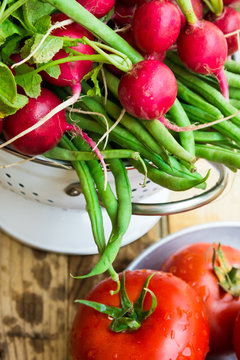 Bunch of fresh organic green beans, red radish in metal colander, ripe tomatoes on wood kitchen table, healthy diet, clean eating, bio produce, authentic natural style