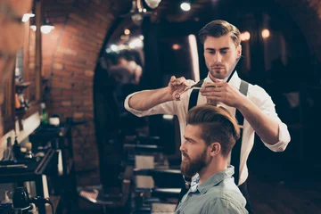 Keuken foto achterwand Kapsalon Profile view of a red bearded stylish barber shop client. He is getting his perfect trendy haircut from a classy dressed handsome stylist, looking in a mirror and waiting for result