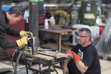 Workers using blow torch in shipyard workshop