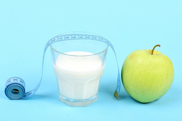 Milk in glass near green apple and tape measure