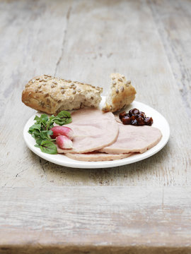 Sliced Danish ham and pickle, garnished with salad leaves and radish with torn seeded rustic bun