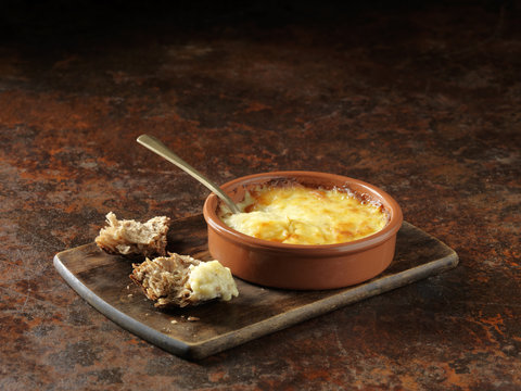 Emmental, Gruyere and Calvados cheese baked in terracotta dish and torn rustic wholemeal bread