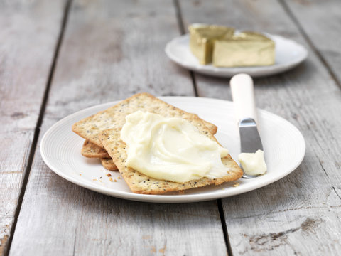 Soft cheese triangles smeared on square crackers with butter knife on plate