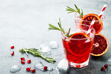 Red cocktail with blood orange and pomegranate. Refreshing summer drink on gray stone or concrete background. Holiday aperitif for Christmas party. Copy space