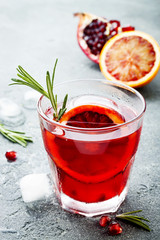 Red cocktail with blood orange and pomegranate. Refreshing summer drink on gray stone or concrete background. Holiday aperitif for Christmas party.
