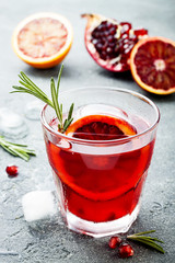 Red cocktail with blood orange and pomegranate. Refreshing summer drink on gray stone or concrete background. Holiday aperitif for Christmas party.
