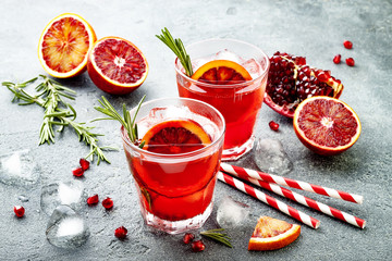 Red cocktail with blood orange and pomegranate. Refreshing summer drink on gray stone or concrete background. Holiday aperitif for Christmas party.
