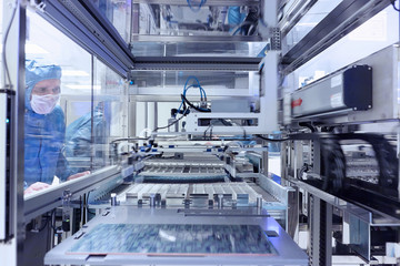 Male worker looking through window of manufacturing machinery in flexible electronics factory clean room