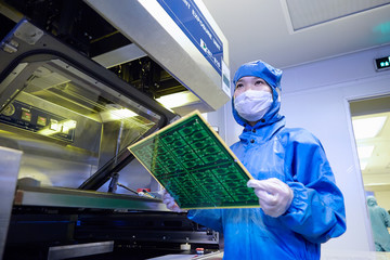 Female worker removing flex circuit from machine in flexible electronics factory clean room