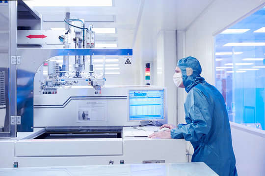 Male worker monitoring manufacturing machinery in flexible electronics factory clean room