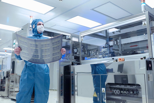 Male worker holding flex circuit in flexible electronics factory clean room