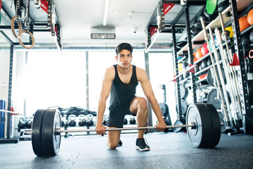 Fototapeta na wymiar Young fit hispanic man in gym lifting heavy barbell
