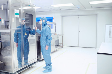 Male worker inspecting manufacturing machinery in flexible electronics factory clean room