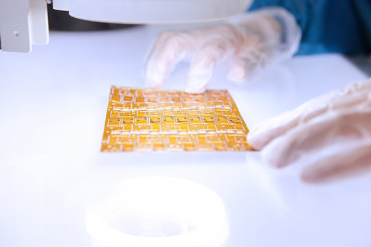 Hands of female worker examining flex circuit in flexible electronics factory clean room
