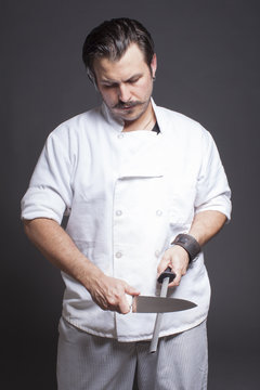 Studio portrait of mid adult male chef sharpening  knife