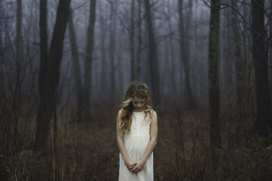 Portrait of long blond haired girl with head bowed in misty forest
