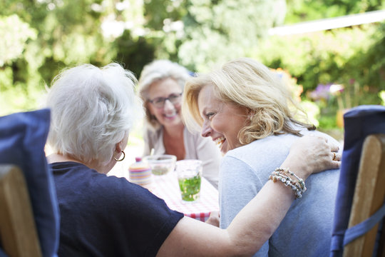 Three women relaxing together in garden, laughing