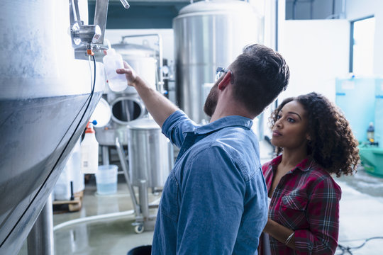 Colleagues in brewery discussing fermentation tank