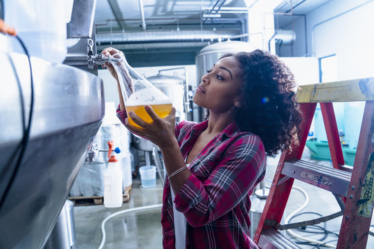 Young woman in brewery filling flask with beer from fermentation tank