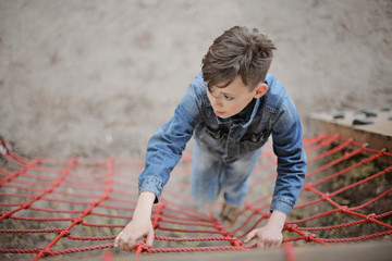 Teenager boy climbing a rope net outdoor on the kid playground. The climber trains simulator on the street.