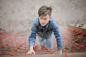 Teenager boy climbing a rope net outdoor on the kid playground. The climber trains simulator on the street.