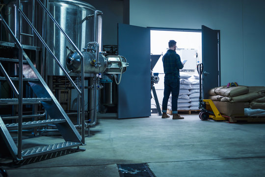 Full length rear view of young man in brewery storage room using digital tablet