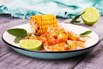 Grilled shrimps and corn garnished with lime and sage leaves. Prawns on white plate